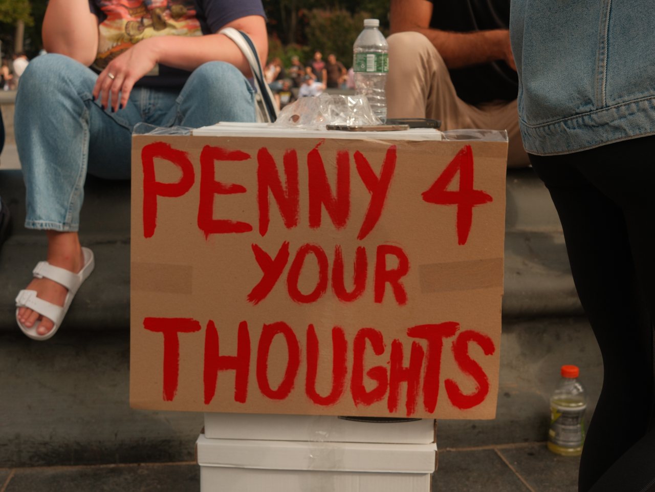 A hand-painted red sign reading Penny 4 Your Thoughts at Washington Square Park.